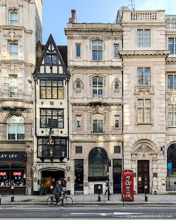 Narrow black-and-white building in London between ornate stone buildings with a red phone box and cyclist