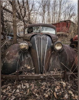 Heavily rusted vintage 1937 Hudson Terraplane car abandoned in woods with bare trees