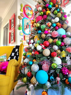 Christmas tree decorated with bright multicolored ornaments in modern living room with yellow couch