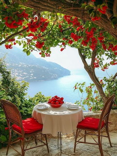Terrace with red chairs under red bougainvillea overlooking blue ocean bay