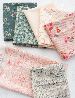 Stack of pastel colored fabric swatches with floral prints and textured patterns on white surface