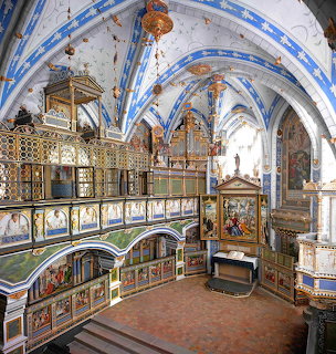 Ornate chapel interior with blue vaulted ceiling, golden organ, painted columns, and decorative balcony