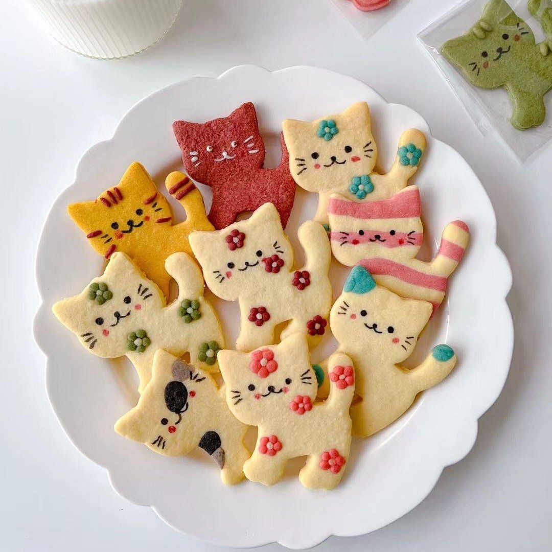 Plate of decorated cat-shaped cookies in yellow, pink, red, and cream with floral icing details