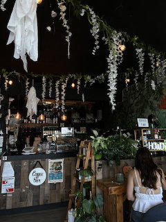 Rustic coffee shop interior with wooden counter, hanging plants, and string lights
