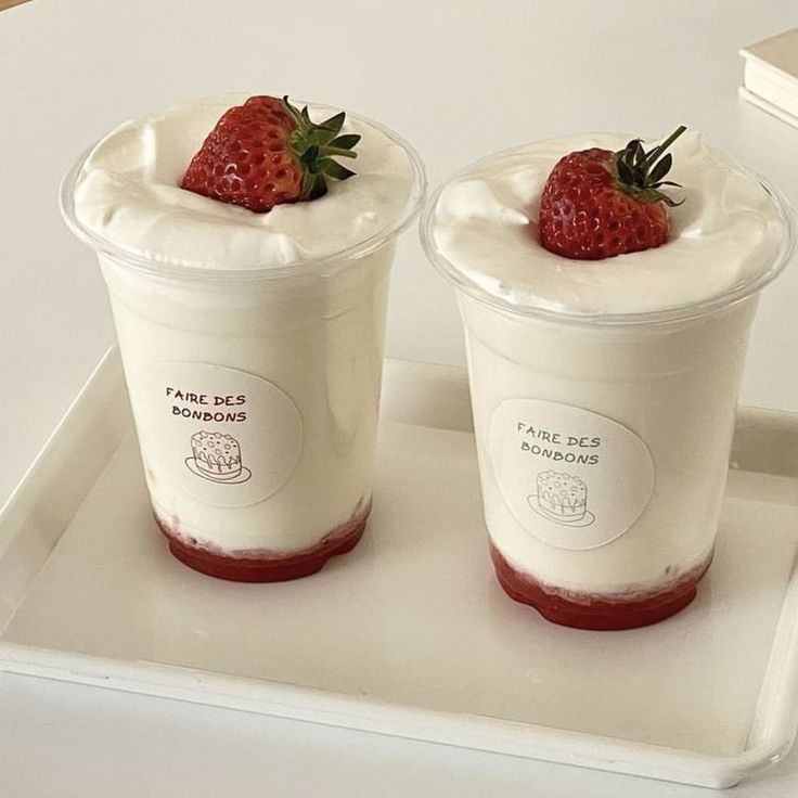 Two dessert cups with strawberry sauce, white cream, and fresh strawberries on top