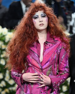 Chappell Roan with long red curly hair and theatrical makeup in a pink sequined jacket at the Met Gala