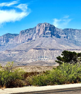 Desert mountain range with steep rocky cliffs and sparse vegetation under blue sky