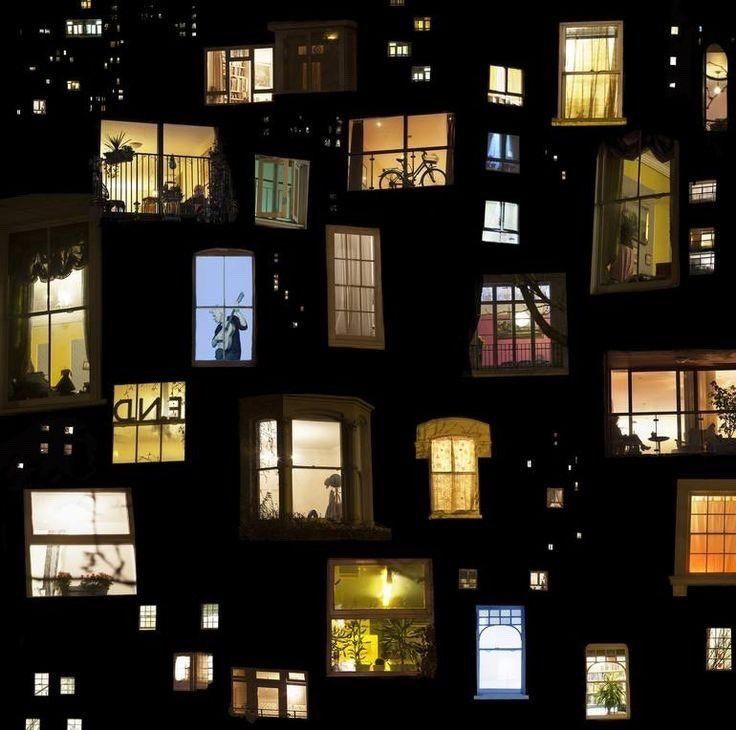 Multiple lit apartment windows at night showing various room interiors and silhouettes against a dark building facade