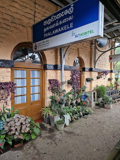 Thalawakele railway station with brick facade, white doors, blue sign, and colorful potted plants on platform