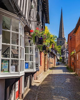 Cobblestone street with timber-framed buildings and hanging flower baskets leading to church spire