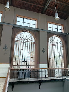 Historic industrial interior with two tall arched windows, metal railings, and exposed wooden ceiling beams