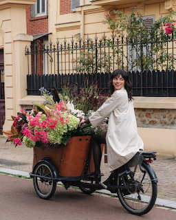 Smiling woman riding a cargo bike loaded with colorful flowers on a quiet street