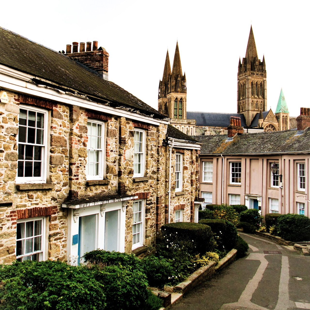 Stone row houses on a curving street with Truro Cathedral's three spires visible behind them