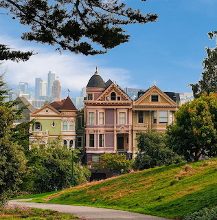 Victorian houses with San Francisco skyline behind, framed by trees and grass