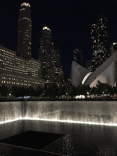 9/11 Memorial reflecting pool at night with illuminated World Trade Center skyscrapers and the Oculus, New York City