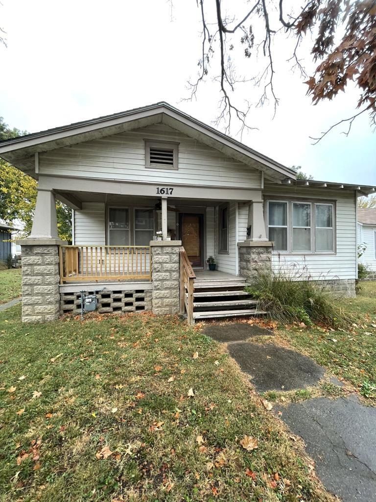 White bungalow house with covered porch, stone pillars, and green lawn in autumn