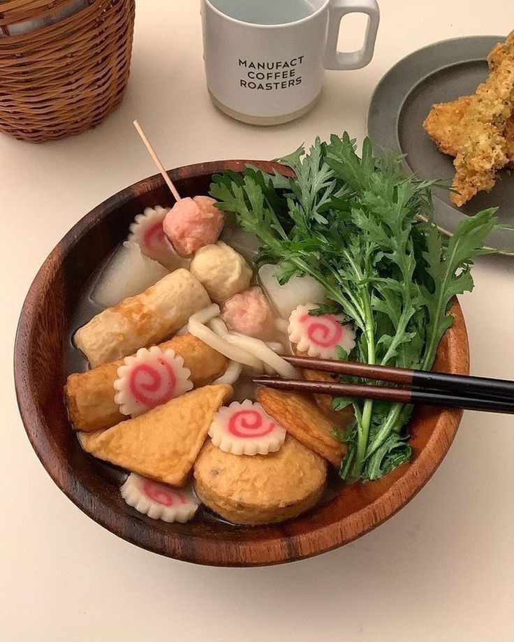 Wooden bowl of Korean oden soup with fish cakes, narutomaki, tofu pouches and greens, with chopsticks