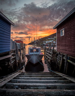 Small boat at a wooden dock between harbor buildings at sunset in Petty Harbour