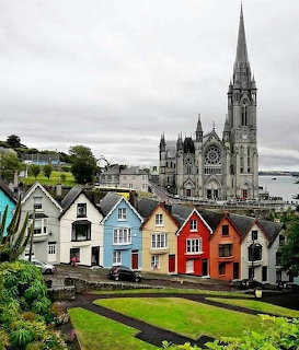 Gothic cathedral with spire towers over colorful pastel houses along waterfront in Cobh, Ireland