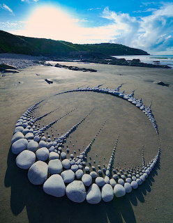 Spiral stone sculpture on beach with white rocks forming curved pattern on sand near ocean