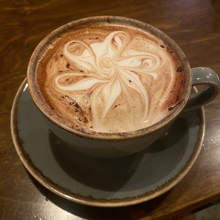 Cup of coffee with flower latte art on a saucer atop a wooden table