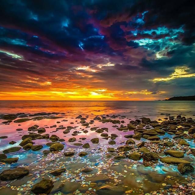 Dramatic sunrise with orange and purple clouds over a rocky beach and ocean