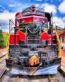 Front view of red locomotive engine 2198 with yellow handrails on railroad tracks under blue sky