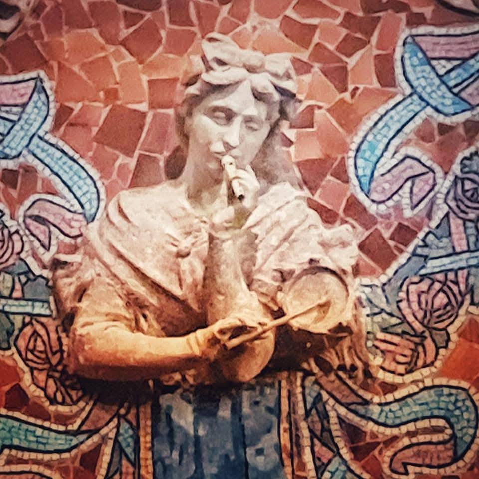 Stone statue of a figure playing a flute surrounded by colorful mosaic tiles