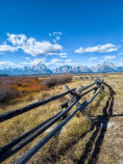 Rustic wooden split-rail fence in golden grassland with Grand Teton mountains and blue sky behind