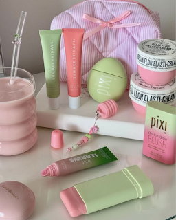 Flatlay of pink and green skincare products including tubes, creams, a candle, and a striped bag