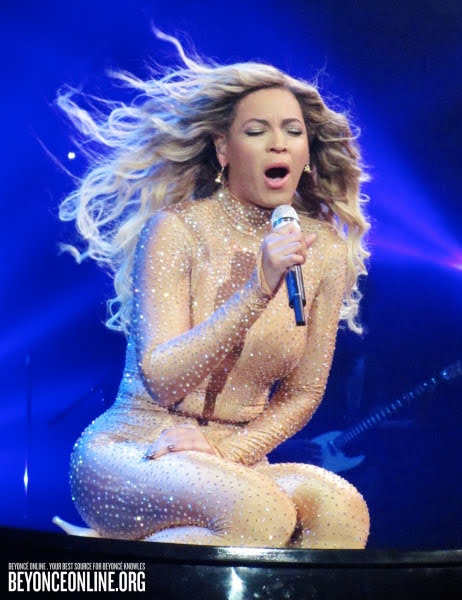 Beyoncé singing on stage in sequined outfit with flowing hair and dramatic blue lighting