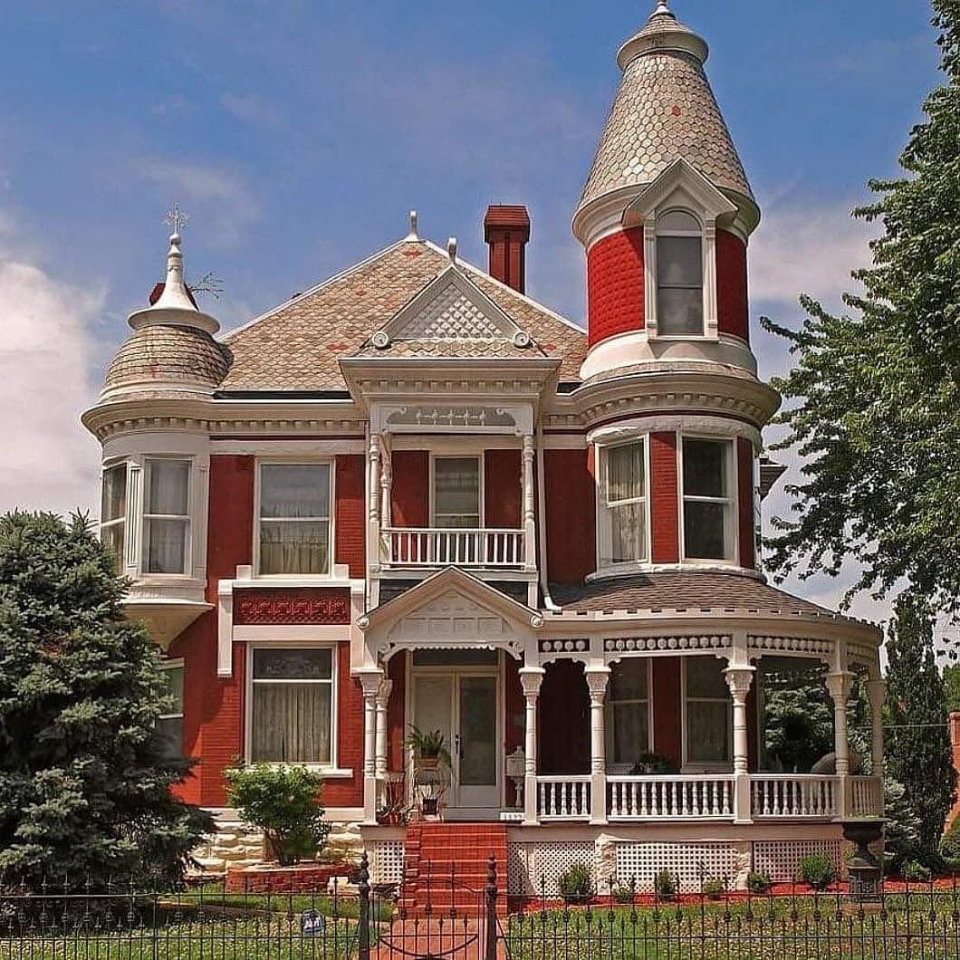 Large Victorian house with turrets, white and red exterior, front porch, surrounded by evergreen trees