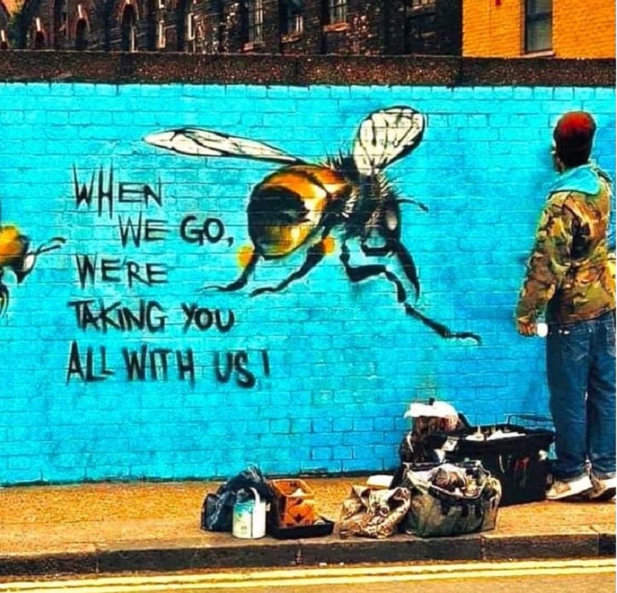 Street art mural of a bee on a blue wall with environmental message and artist standing beside it