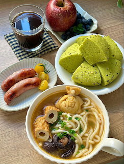 Overhead view of noodle soup, sausages, coffee, green cake, apple, and blueberries on a table