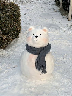 Snowman sculpted to look like a cute polar bear wearing a dark gray scarf on snowy ground