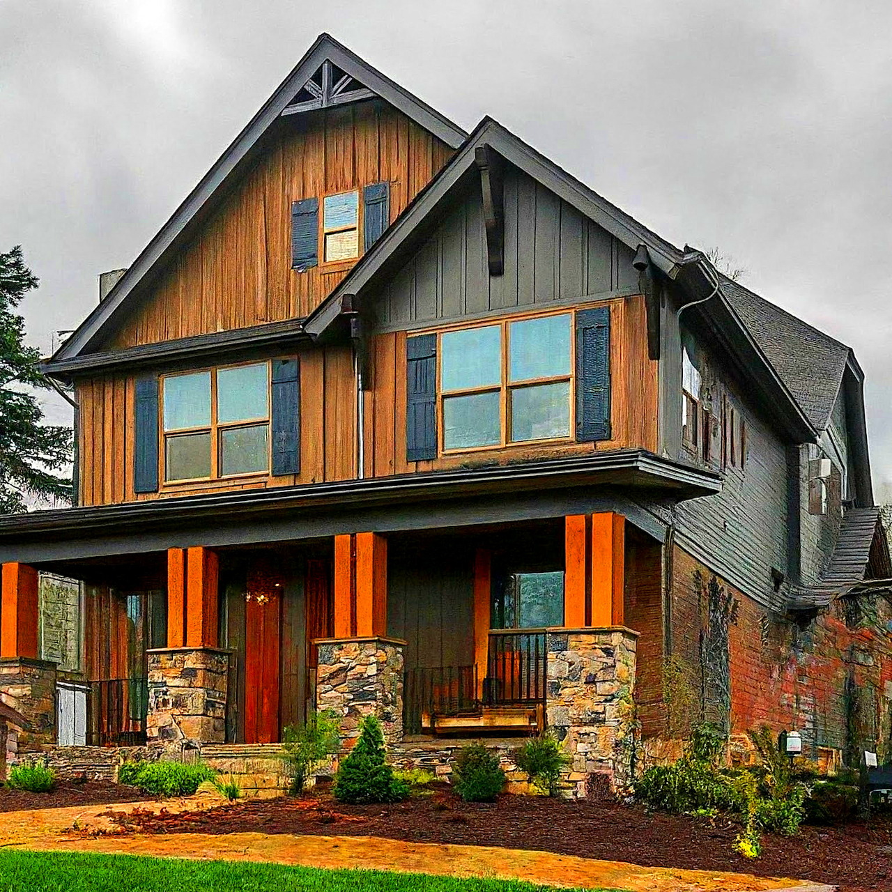 Craftsman house with orange wood siding, stone pillars, and large windows under cloudy sky