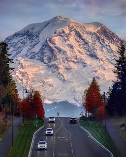 Snow-capped Mt. Rainier rising above highway with fall foliage and vehicles in Washington