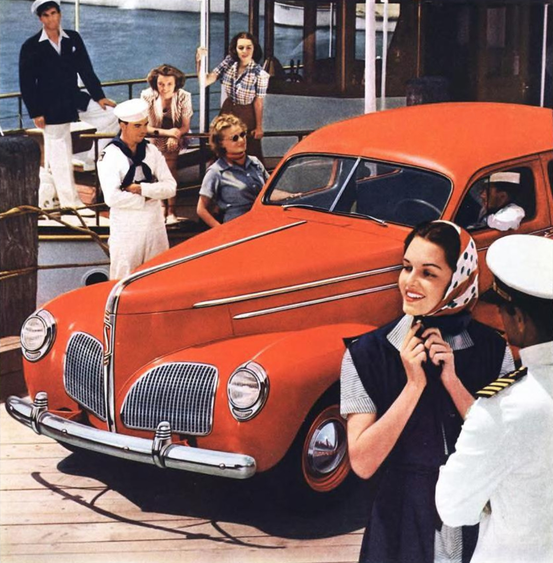 Orange 1940 Studebaker car with people in vintage clothing at waterfront setting