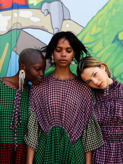 Three girls in colorful gingham dresses posing against a colorful mural background