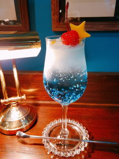 Blue layered cocktail in wine glass with strawberry and star fruit garnish on wooden table