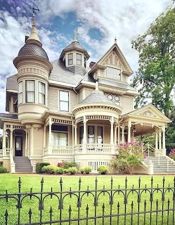 Cream Victorian house with turret, porch, ornate details, garden, and iron fence