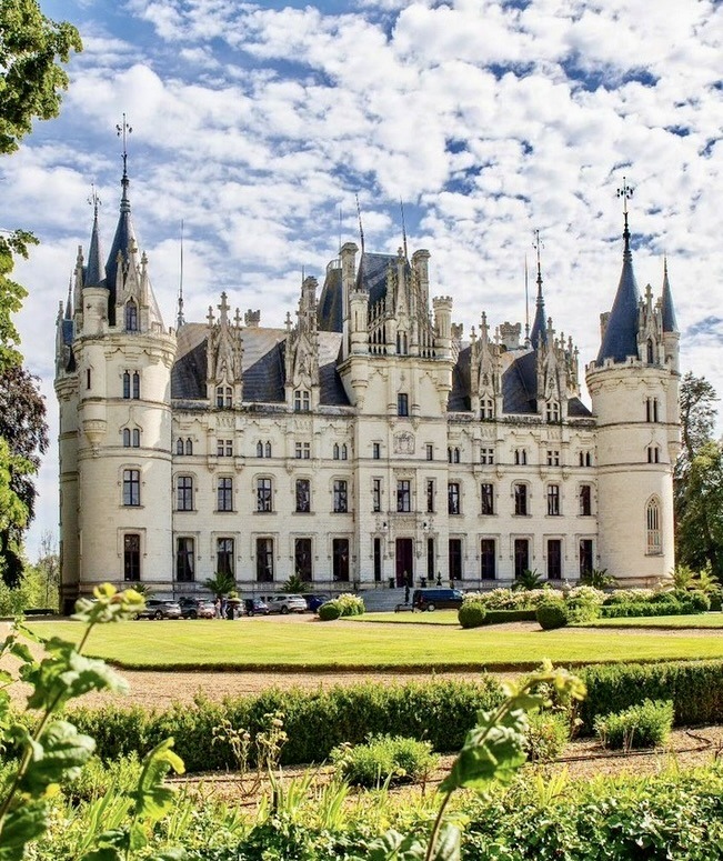 White Gothic Revival French chateau with pointed spires and formal green gardens in foreground