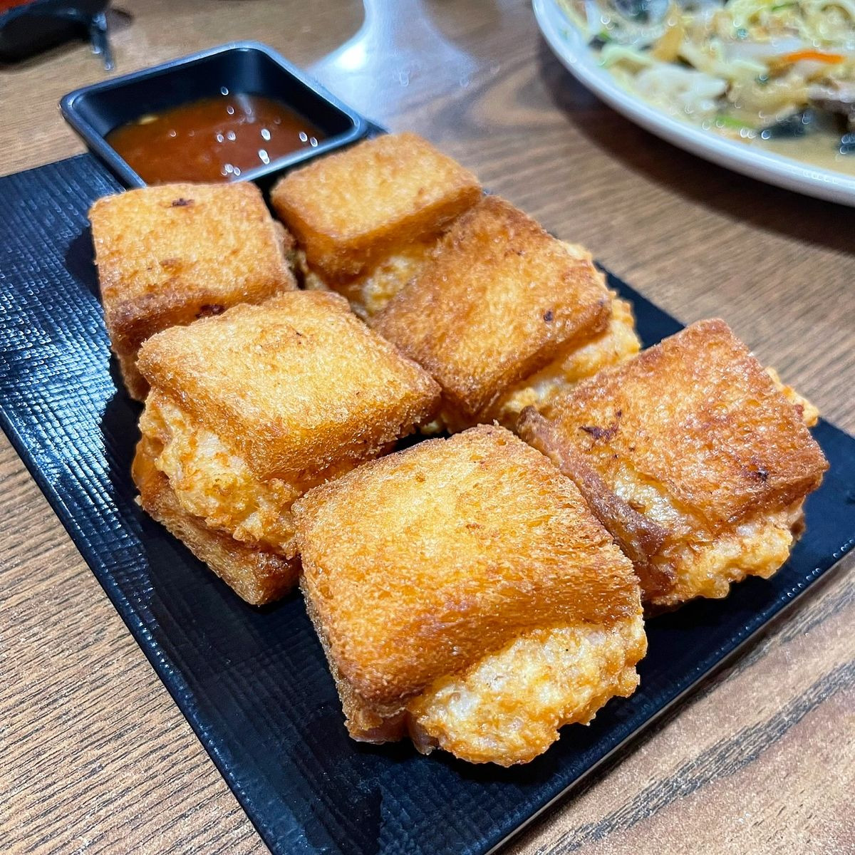 Fried shrimp toast cubes on a black plate with red dipping sauce