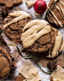 Gingerbread cookies decorated with white icing, red Christmas ball ornament, spices and powdered sugar on wood table