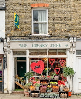 Small brick flower shop with white storefront, plants and flowers displayed outside on urban street