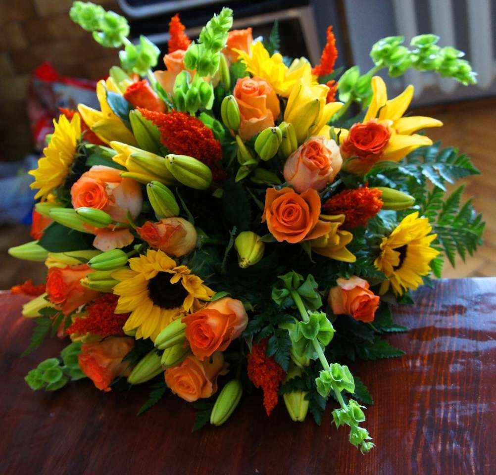 Vibrant bouquet of sunflowers, orange roses, yellow lilies, and green flowers on wooden table