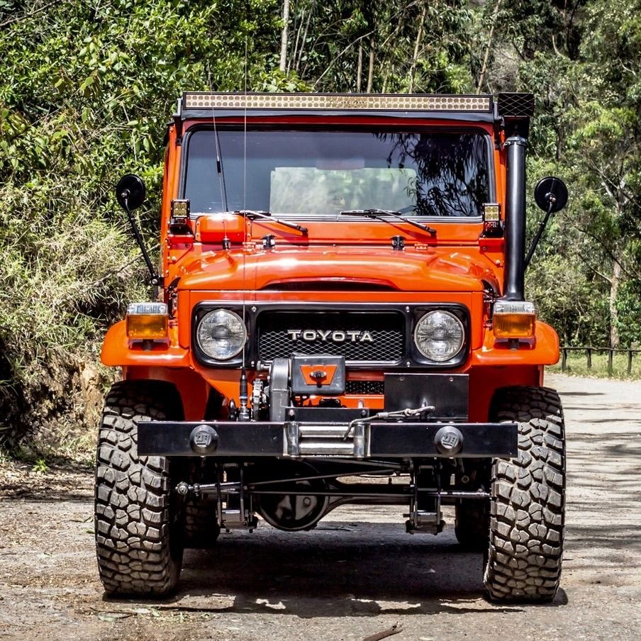 Front view of an orange Toyota off-road vehicle with large tires on a dirt road