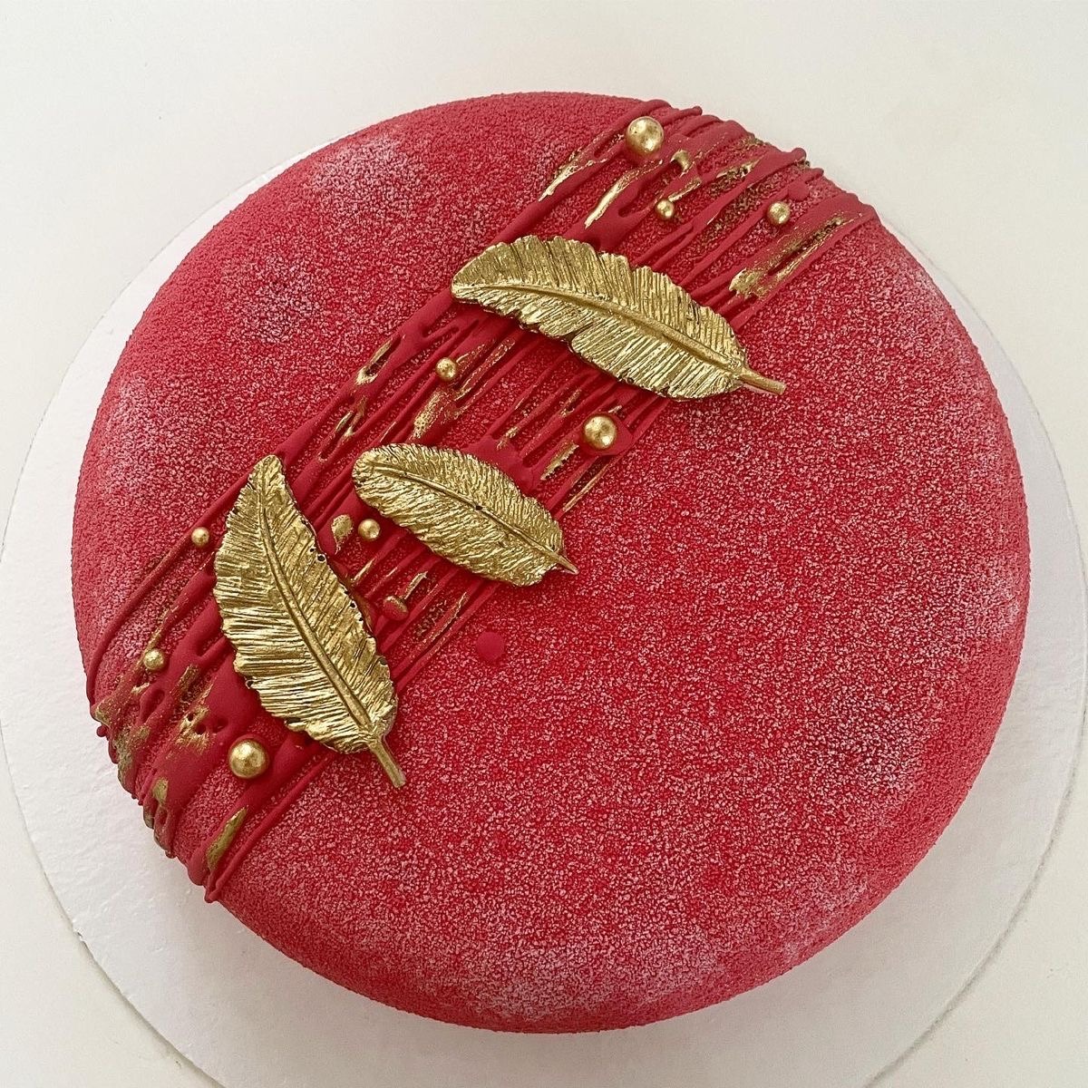 Round red cake decorated with gold leaves and drizzle on a white background