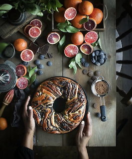 Overhead view of a swirl cake on a table with citrus fruit, plums, and baking utensils