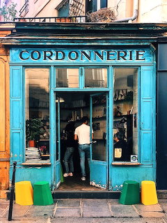 Person entering bright blue Cordonnerie shop with yellow and green bollards on Parisian street